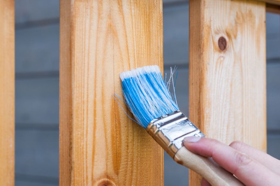 A hand painting a wooden plank with a blue brush.